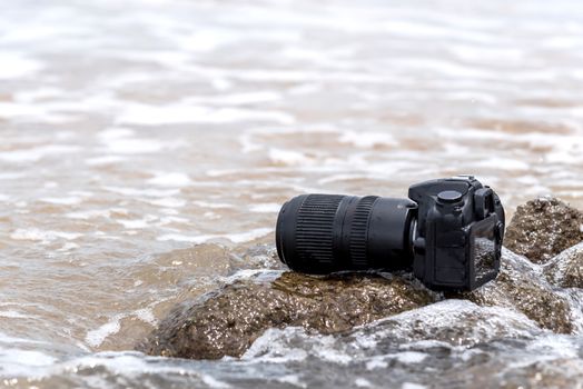 DSLR camera with telephoto lens wet from water sea wave at stone beach when travel and test using in the extreme environment demo waterproof by photographer