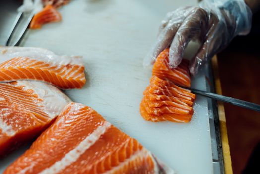 Asian chef slice salmon by knife on boad for japanese food delicacy consisting sashimi salmon of very fresh raw salmon fish sliced into thin pieces serving with radish sliced in japanese restaurant