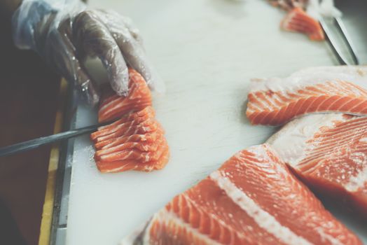 Asian chef slice salmon by knife on boad for japanese food delicacy consisting sashimi salmon of very fresh raw salmon fish sliced into thin pieces serving with radish sliced in japanese restaurant