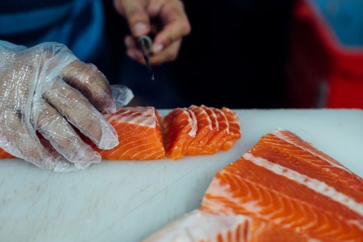 Asian chef slice salmon by knife on boad for japanese food delicacy consisting sashimi salmon of very fresh raw salmon fish sliced into thin pieces serving with radish sliced in japanese restaurant