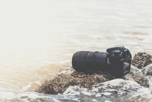 DSLR camera with telephoto lens wet from water sea wave at stone beach when travel and test using in the extreme environment demo waterproof by photographer