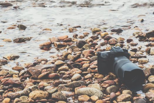 DSLR camera with telephoto lens wet from water sea wave at stone beach when travel and test using in the extreme environment demo waterproof by photographer