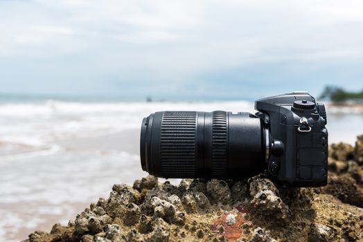 DSLR camera with telephoto lens wet from water sea wave at stone beach when travel and test using in the extreme environment demo waterproof by photographer