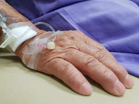 Patient asian elder women 80s with saline intravenous at C-line or A-line on a elderly patient hand on patient bed in intensive care unit (ICU.) room at hospital.