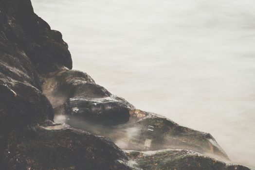 DSLR camera with telephoto lens wet from water sea wave at stone beach when travel and test using in the extreme environment demo waterproof by photographer