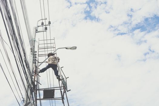 Electricians or handyman or worker risk working to install electric line on high pole by scaffolding on pickup truck at Bangkok Thailand.