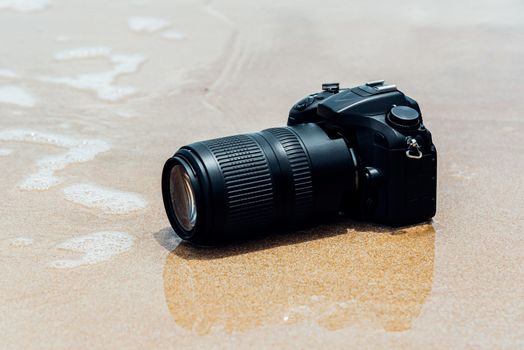 DSLR camera with telephoto lens on a beach it wet from water sea wave when travel and test using in the extreme environment demo waterproof by photographer