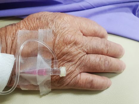 Patient asian elder women 80s with saline intravenous at C-line or A-line on a elderly patient hand on patient bed in intensive care unit (ICU.) room at hospital.