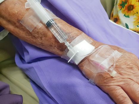 Patient asian elder women 80s with saline intravenous at C-line or A-line on a elderly patient hand on patient bed in intensive care unit (ICU.) room at hospital.