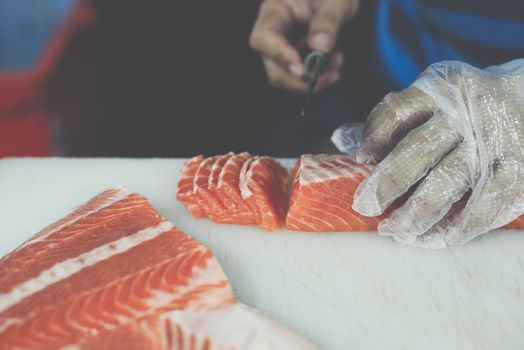 Asian chef slice salmon by knife on boad for japanese food delicacy consisting sashimi salmon of very fresh raw salmon fish sliced into thin pieces serving with radish sliced in japanese restaurant