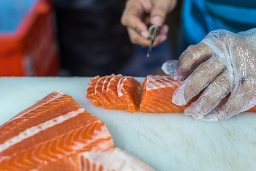 Asian chef slice salmon by knife on boad for japanese food delicacy consisting sashimi salmon of very fresh raw salmon fish sliced into thin pieces serving with radish sliced in japanese restaurant