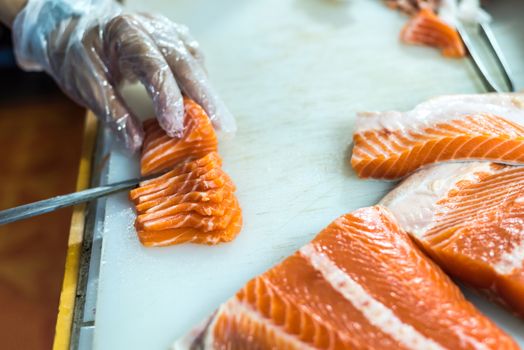 Asian chef slice salmon by knife on boad for japanese food delicacy consisting sashimi salmon of very fresh raw salmon fish sliced into thin pieces serving with radish sliced in japanese restaurant