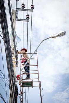 Electricians or handyman or worker risk working to install electric line on high pole by scaffolding on pickup truck at Bangkok Thailand.