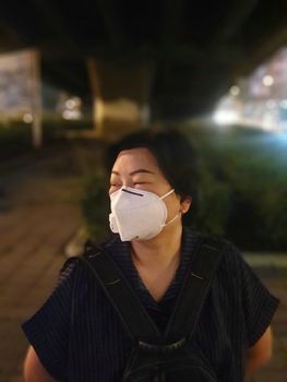 Asian woman use mask N95 respiratory protection mask against air with smog PM2.5 dust exceed the standard value of Bangkok city with bad weather air pollution on road with traffic in Bangkok