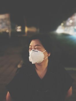 Asian woman use mask N95 respiratory protection mask against air with smog PM2.5 dust exceed the standard value of Bangkok city with bad weather air pollution on road with traffic in Bangkok