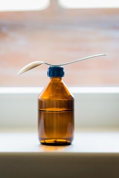 A cough syrup bottle with a spoon close to the window