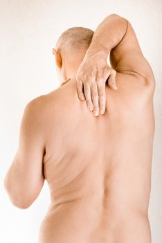 Man massaging his top back, between the shoulders, because of a thoracic vertebrae pain due to a displacement of a dorsal vertebra rubbing on a nerve