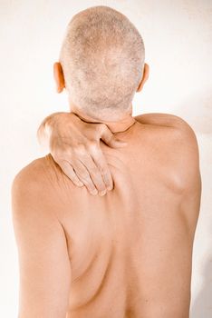 Man massaging his top back, the trapezius muscle, because of a thoracic vertebrae pain due to a displacement of a dorsal vertebra rubbing on a nerve