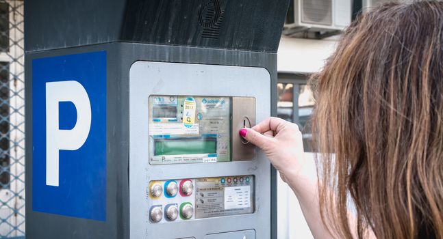 Albufeira, Portugal - May 3, 2018: Woman in front of a parking ticket machine paying her parking in the city center on a spring day