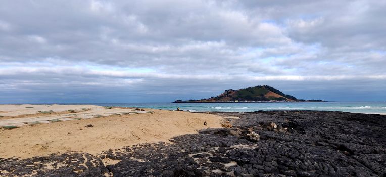 Black volcanic rock in Hyeopjae beach with mountain and cobalt blue sea in Jeju Island, South Korea