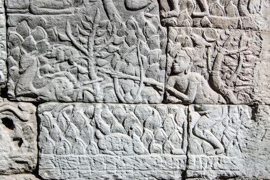 Ancient Khmer carving of a man hunting a deer in the woods with a rabbit nibbling the grass. Wall of Bayon Temple, Angkor Thom, Siem Reap, Cambodia.