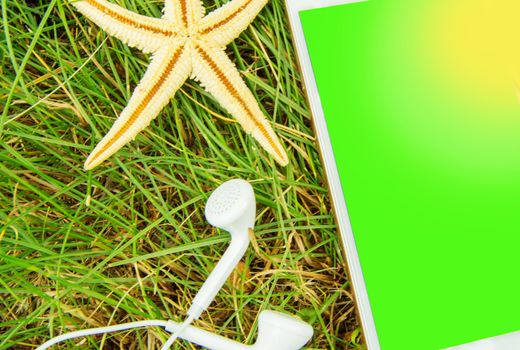 The concept of booking hotels and vacations using a mobile phone, headphones, phone and starfish on the green grass. Chromakey green screen of a mobile phone.