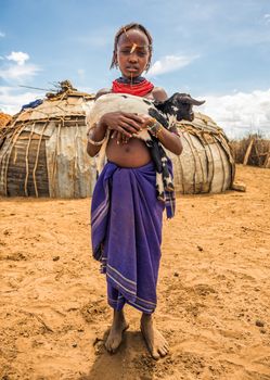 OMO VALLEY, ETHIOPIA - MAY 6, 2015 : Girl from the African tribe Dasanesh holding a goat in her village.