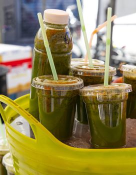 Close up fresh green fruit and vegetable juice in plastic bottles and glasses with drinking straws at retail display, low angle side view