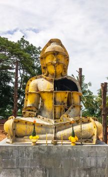 Casting mold a statue of Buddha in a yellow metal structure with the use of cement there are trees and the sky is the background.