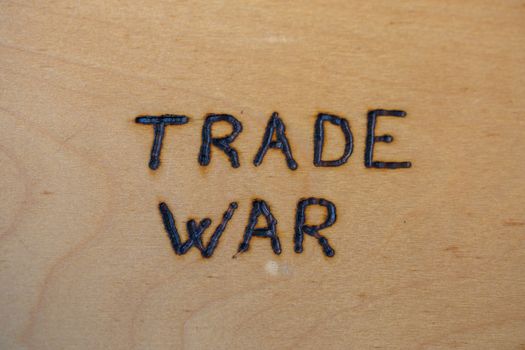 the words trade war handwritten on flat bare plywood surface with woodburner.