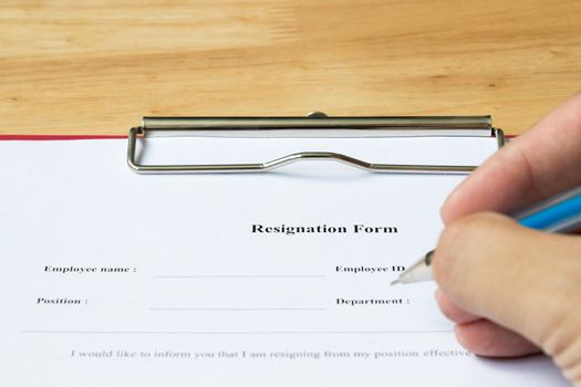 Resignation form with hand hold the pen for filling on wood desk background