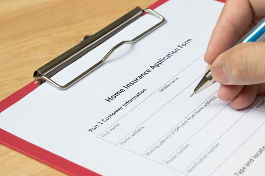 Mand fill the home insurance application form with red file on wooden table