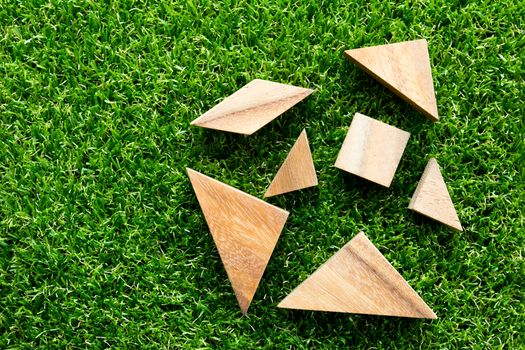 Wooden tangram puzzle wait for complete on artificial green grass background