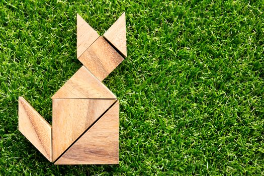 Wooden tangram puzzle in cat shape on artificial green grass background
