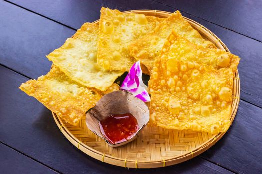 Yellow fried dumplings and a cup of sauce on a bamboo dish at decorated with orchid placed on the table dark wood.