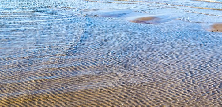 Detailed close up view on water surfaces with waves and ripples and the sunlight reflecting at the surface