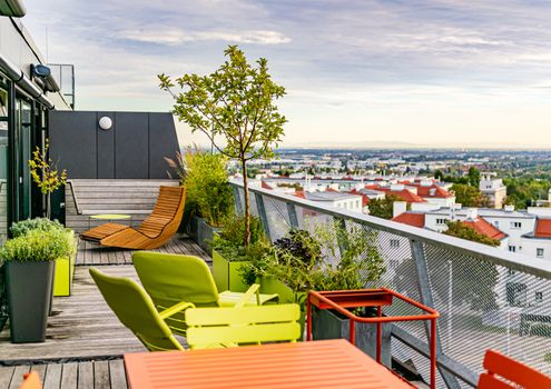 Outdoor furniture on a rooftop terrace with a cloudy sky and an overview over the south of Vienna