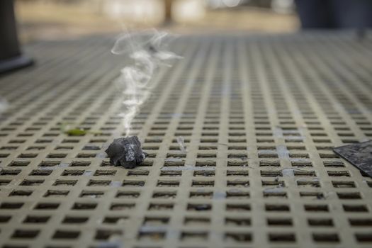 Smoke emitted from a piece of burnt wood coal on a metal table. Close up with selective focus.