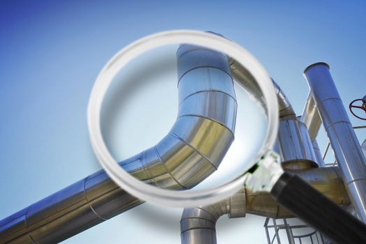 Geothermal stainless steel power pipe structure of a geothermal power station against a sky background - Concept image seen through a magnifying glass.