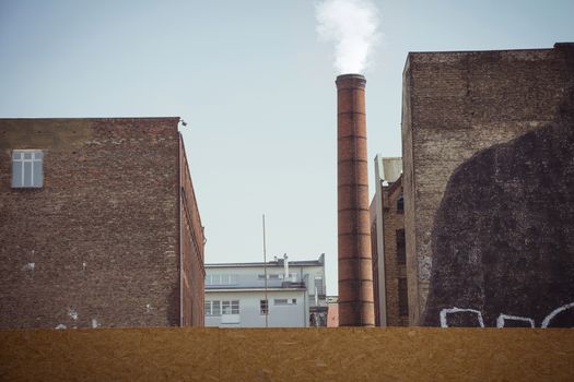 Smoke emitted from an industrial brick chimney in an old factory building. It located in Berlin, Germany.