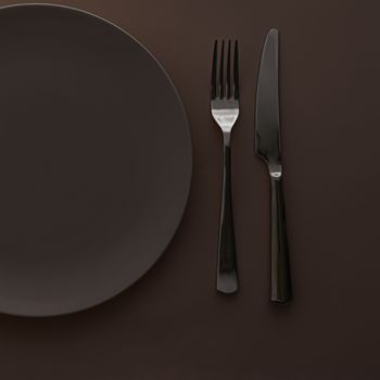 Empty plate and cutlery as mockup set on dark brown background, top tableware for chef table decor and menu branding design