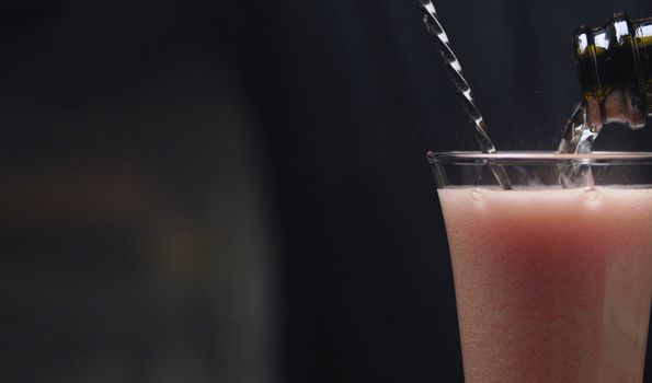 Making Strawberry Rossini Cocktail. Close up bartenders hands pouring champagne into a glass with crushed strawberries.