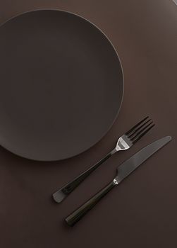 Empty plate and cutlery as mockup set on dark brown background, top tableware for chef table decor and menu branding design