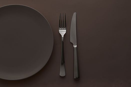 Empty plate and cutlery as mockup set on dark brown background, top tableware for chef table decor and menu branding design