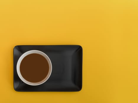 Chocolate bowl on a black tray. Yellow background. Minimalist image from above with space available to copy text.Top view.