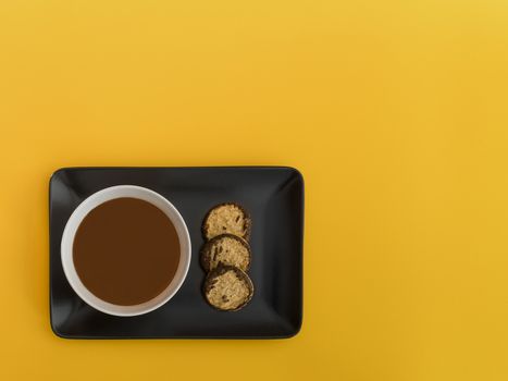 Chocolate bowl on a black tray. Yellow background. Minimalist image from above with space available to copy text. Top view.