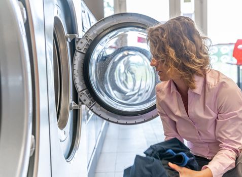 inserting dirty clothes into the washing machine in the laundry room.