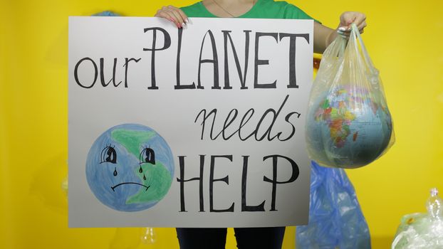 Unrecognizable woman girl volunteer in t-shirt with recycle logo with protesting poster Our Planet Needs Help and globe in plastic package. Save ecology environment. Plastic trash nature pollution