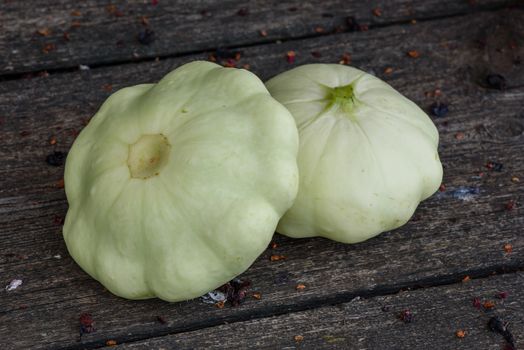 Two ripe pattypan squash lie on the old wooden table in the garden