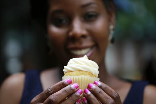 Close up of African American women's hands holding cupcake - selective focus on cupcake with blurred face on background
